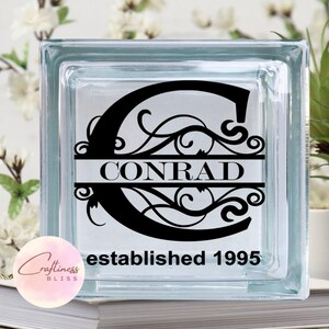 May include: A clear glass block with a black vinyl decal featuring a stylized letter C with a decorative flourish and the name "CONRAD" centered below. The text "established 1995" is printed below the name.