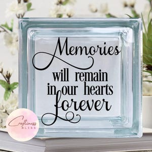 May include: A glass block with the text "Memories will remain in our hearts forever" in black lettering. The block is clear and has a frosted finish.