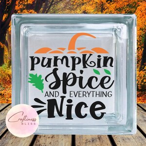 May include: A clear glass block with the words "pumpkin spice and everything nice" in black script and a pumpkin graphic in orange. A green leaf graphic is also included. The block is on a wooden surface.