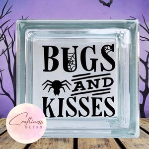 May include: A glass block with a black and white design that says "Bugs and Kisses" with a spider graphic.