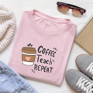 May include: A light pink t-shirt with the words "Coffee Teach Repeat" and a coffee cup graphic. The shirt is folded and surrounded by other items, including sunglasses, a notebook, and sneakers.