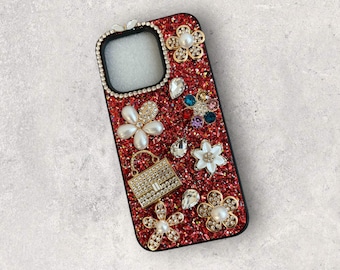 Op de afbeelding: Rode glitter telefoonhoes met zwarte rand, versierd met parel- en strassbloemen, een kleine handtas en diverse edelstenen. Ontworpen voor een smartphone.