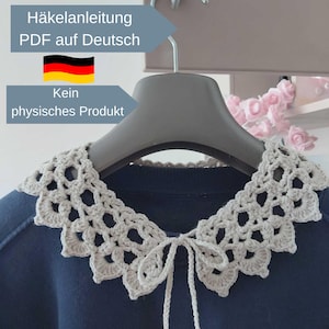 Könnte beinhalten: Ein hellgrauer, gehäkelter abnehmbarer Kragen mit gewelltem Rand und einer dünnen Bindeschleife in der Mitte. Der Kragen liegt auf einem dunkelblauen Kleidungsstück auf einem Kleiderbügel. Text: Häkelanleitung PDF auf Deutsch und Kein physisches Produkt.
