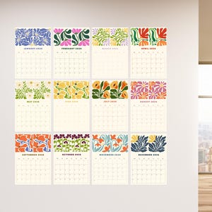May include: A collection of twelve 2020 calendars, each with a unique floral pattern at the top. The calendars are displayed in a grid on a white wall. The floral designs incorporate various colours, such as blue, pink, yellow, and orange.