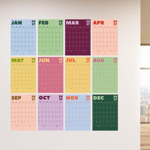 May include: A 2027 wall calendar set featuring twelve individual monthly pages in distinct colours including light blue, green, dark purple, peach, yellow, pink, gold, light green, tan, lavender, sky blue, and dark green with grid layouts.