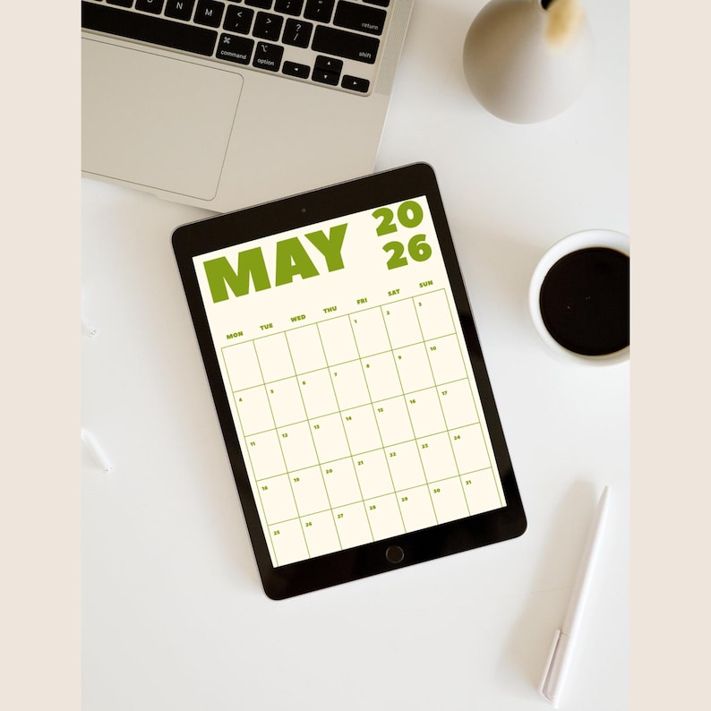 May include: A black tablet showing a May 2026 calendar, with green text. The tablet is on a white surface, with a laptop, a coffee cup, a pen, and a decorative vase. The calendar is a useful tool for planning.