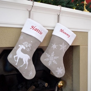 May include: Two Christmas stockings, one embroidered with "Hattie" and the other with "Mummy" in red. They are grey with white cuffs. One has a white reindeer, the other snowflakes. Festive decorations for the holiday season.