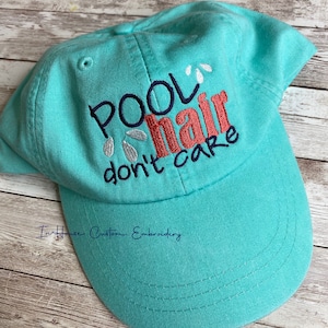 May include: A turquoise blue baseball cap with white and navy blue embroidery that reads "Pool Hair Don't Care".