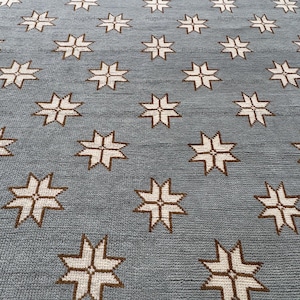 May include: A blue rug featuring a repeating starburst design in white and brown. The rug has a textured surface and a border. The starbursts are evenly spaced across the rug's surface, creating a symmetrical pattern.