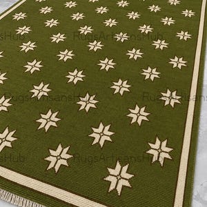Op de afbeelding: Een rechthoekig olijfgroen tapijt met een herhalend patroon van crèmekleurige sterren. Het tapijt heeft een crèmekleurige rand en franjes langs de onderkant. De woorden "Rugs Artisans Hub" zijn zichtbaar in de afbeelding.