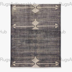 Op de afbeelding: Een rechthoekig, donkergrijs tapijt met een geometrisch patroon. Het ontwerp bevat ruit- en pijlvormen in een lichtere beige kleur, verbonden door dunne, rechte lijnen. Het tapijt heeft een verweerde, vintage uitstraling.