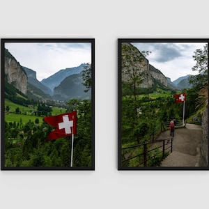 Könnte beinhalten: Zwei gerahmte Drucke einer Schweizer Berglandschaft, jeweils mit einer roten Flagge mit weißem Kreuz. Die Bilder zeigen ein grünes Tal, Klippen und eine Person, die auf einem Pfad geht. Die Drucke sind in Schwarz gerahmt.