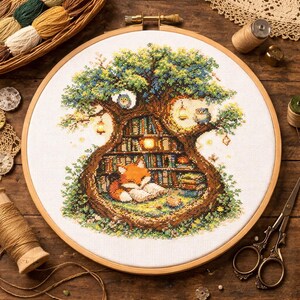 以下が含まれることがあります： 図書館のある木をクロスステッチ刺繍で表現。眠っているキツネが特徴です。木は緑と青のキャノピーで、フクロウとランタンがあります。キツネはオレンジと白で、枕の上にいます。刺繍は木の枠に入っています。