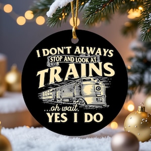 May include: Black round Christmas ornament with gold string. The ornament features the text "I DON'T ALWAYS STOP AND LOOK AT TRAINS...oh wait, YES I DO" with a train illustration in cream color.