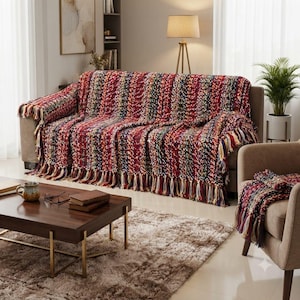 Puede incluir: Una manta de punto grueso multicolor con rayas verticales de hilo rojo, azul oscuro, verde y amarillo. La manta tiene una apariencia tejida y texturizada con largos flecos decorativos a lo largo del borde inferior.