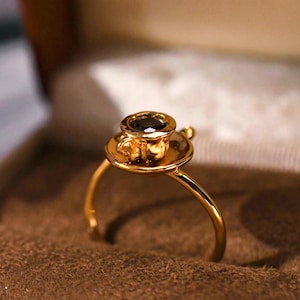 Könnte beinhalten: Eine weiße Keramik-Tasse mit schwarzem Henkel und dem Text "But First, Coffee" in schwarzer, fetter Schrift. Die Tasse steht auf einer weißen Oberfläche.