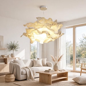 May include: A large, cream-coloured pendant light fixture with a multi-layered, ruffled fabric shade that creates a soft, diffused glow. The light is suspended from the ceiling by a thin cord attached to a circular, white mounting canopy.