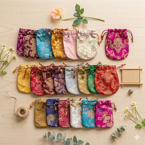 Könnte beinhalten: Eine Sammlung farbenfroher, gemusterter Kordelzugbeutel in verschiedenen Farben, darunter Rosa, Blau, Gold und Lila. Jeder Beutel hat ein dekoratives Blumen- oder Paisley-Design. Die Beutel liegen auf einer hellen Holzoberfläche.