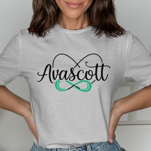 May include: A light grey t-shirt featuring the word "Avascott" in a cursive font, above a teal infinity symbol. The design is in black and teal. The shirt is made of a soft material.