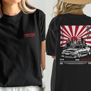 May include: Black t-shirt with the word "TOKYO" in red script on the front. The back features a graphic of a car in front of a cityscape with a rising sun design and Japanese text.