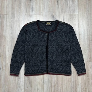 Pode incluir: Cardigã cinza escuro com um design estampado. O cardigã tem decote redondo e mangas compridas. As bordas são aparadas com uma borda vermelha e verde. A marca "OLEANA" é visível em uma etiqueta perto da gola.