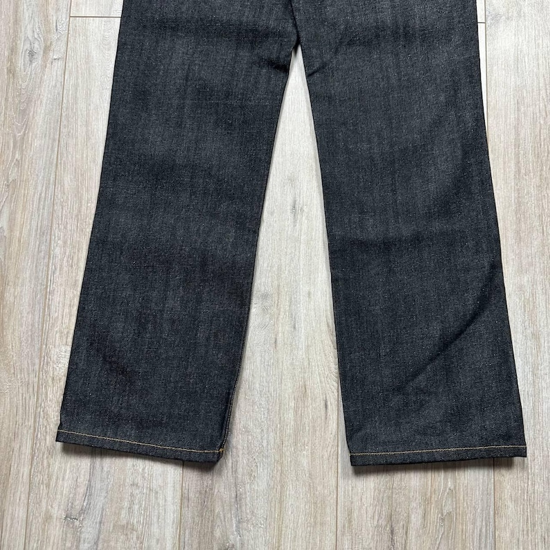 May include: Dark wash denim jeans with a straight leg cut. The jeans have a classic five-pocket design and a button and zipper closure. The hem is finished with a contrasting yellow stitch.