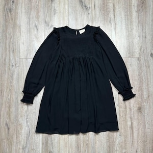 May include: Black long-sleeve dress with a round neckline and pleated bodice. The dress features ruffled detailing at the shoulders and elastic cuffs. The dress is made of a lightweight fabric and has a flowing silhouette.