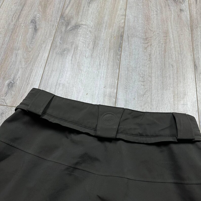 May include: A white ceramic mug with a black handle and the text "But First, Coffee" in a bold, black font. The mug is set against a blurred background, suggesting a cozy setting.