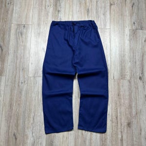 May include: Solid navy blue trousers featuring a relaxed, straight-leg silhouette. The trousers are designed with an elasticated waistband that includes a functional drawstring tie at the centre front for an adjustable fit and a simple, clean finish.