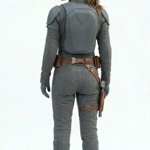 May include: A gray jumpsuit with a matching vest and boots. The vest has a winged emblem. A brown belt and holster are visible. The person is wearing gloves and has their hair in a ponytail.