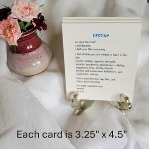 May include: A deck of 48 cards with the word "DESTINY" printed on each card. Each card measures 3.25" x 4.5". The text on the card includes affirmations about life, health, and happiness. A small vase with pink and burgundy flowers is in the background.