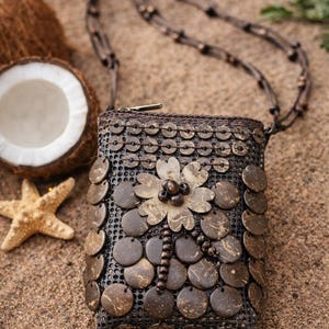 May include: A small, rectangular brown purse with a flower design made of circular wooden pieces. The purse has a long, beaded strap and a zipper closure. A starfish and a coconut are in the background.