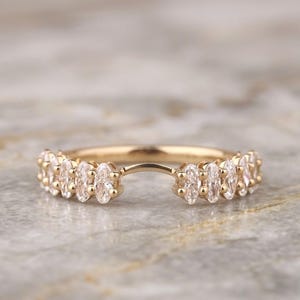 Peut inclure: Une bague en or au design incurvé, ornée d'une série de pierres claires taillées en marquise. La bague présente une ouverture centrale, avec les pierres disposées le long des côtés de l'anneau, créant une apparence symétrique et arquée.