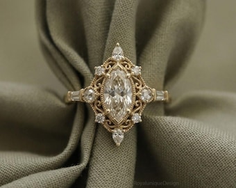 May include: A gold ring featuring a central marquise-cut stone surrounded by smaller round and pear-shaped stones in a filigree setting. The band includes baguette-cut stones on each side. The text RoyaluniqueDesign is visible at the bottom.