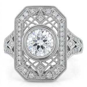 May include: A silver-toned ring featuring a large, round, brilliant-cut center stone set in a circular bezel. The rectangular frame surrounding the center stone is decorated with intricate openwork metal filigree and numerous small, round, clear pavé-set stones.