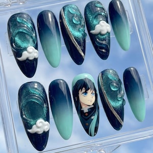 May include: A set of ten artificial nails in a clear plastic case. The nails feature a gradient design from dark blue to teal, with accents of silver and white cloud-like shapes. One nail has a character illustration.