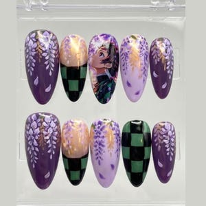 May include: A set of ten almond-shaped false nails. The nails feature various designs, including wisteria flowers, a character illustration, and a green and black checkered pattern. The color palette includes purple, gold, and green.