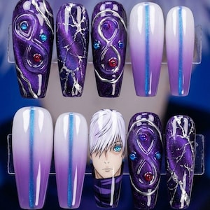 May include: A set of ten artificial nails in a clear plastic case. The nails feature a variety of designs, including purple marble, blue and red gem accents, and a character face. The nails are in various shades of purple and white.