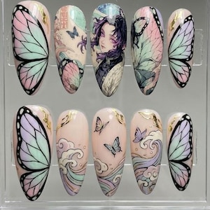 Puede incluir: Un conjunto de diez uñas artificiales con varios diseños. Las uñas presentan patrones de alas de mariposa, arte de personajes de anime y motivos japoneses de olas y mariposas. Los colores incluyen rosa, morado, azul y detalles dorados. Las uñas se muestran en una caja de plástico transparente.