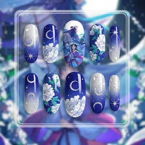 May include: A set of ten artificial nails with a blue and white design. The nails feature various patterns, including moons, stars, floral motifs, and an illustration of figures in traditional clothing. The nails have an oval shape and a glossy finish.