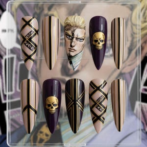 May include: A set of ten long, almond-shaped false nails. Designs include gold and black geometric patterns, a portrait of a man with blonde hair, and a gold skull on a dark purple background. The nails are displayed in a clear plastic case.
