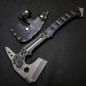 Könnte beinhalten: Eine taktische Axt mit schwarzem Griff und silberner Klinge, zusammen mit einer schwarzen Lederscheide. Die Axt verfügt über einen Hammerkopf und eine scharfe Klinge, konzipiert für den Outdoor- und Survival-Einsatz.
