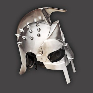 May include: A silver-colored helmet with a pointed top and multiple conical spikes. The helmet has a visor and cheek guards, and is likely made of metal. The design suggests a medieval or fantasy theme.