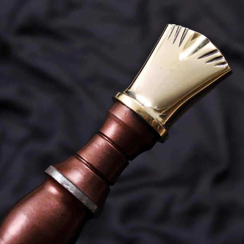 Pode incluir: Close-up de uma rolha de garrafa decorativa. A rolha apresenta um topo dourado em forma de leque e uma pega cor de cobre com detalhes prateados. O design &eacute; detalhado e elegante, adequado para garrafas de vinho.