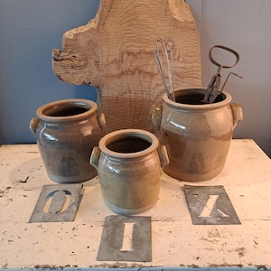 Op de afbeelding: Een set van drie keramische mokken met een gespikkelde, matte afwerking. De mokken zijn in crème, lichtgrijs en donkergrijs. Elke mok heeft een eenvoudig, minimalistisch ontwerp en een afgeronde handgreep.