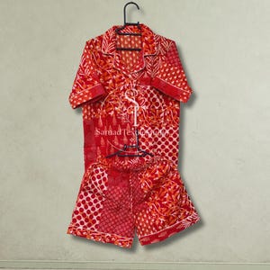 May include: A two-piece pajama set featuring a short-sleeved button-down shirt and matching shorts in a vibrant red and orange patchwork pattern. The fabric displays various geometric and floral prints. A logo reads SamadTextileStudio.