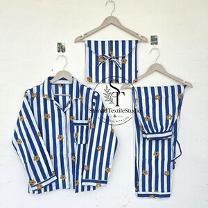 Op de afbeelding: Blauw en wit gestreepte pyjamaset met een bloemenpatroon. De set bevat een overhemd met knopen, een broek en een bijpassend etui, allemaal opgehangen aan houten kleerhangers. De pyjama heeft een klassiek ontwerp.