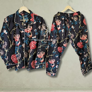 May include: A black pajama set featuring a long-sleeved button-down shirt and matching pants, both decorated with a vibrant floral pattern of red, pink, and teal flowers on dark branches. The shirt includes white piping along the collar and cuffs.