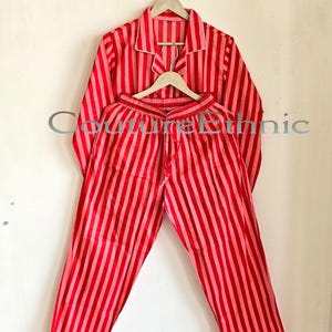 May include: Red and pink striped pajama set. The long-sleeved top and pants are made of a soft fabric and feature vertical stripes. The top has a collared neckline and white trim. The pants have a drawstring waist.