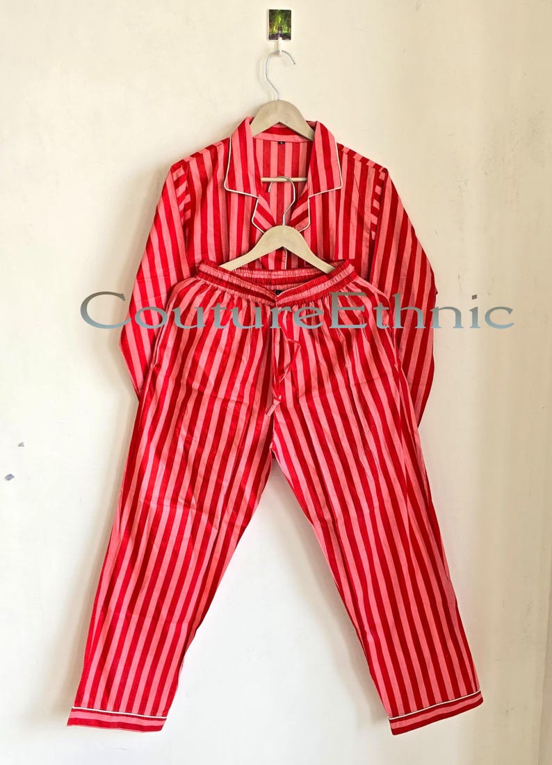 May include: Red and pink striped pajama set. The long-sleeved top and pants are made of a soft fabric and feature vertical stripes. The top has a collared neckline and white trim. The pants have a drawstring waist.